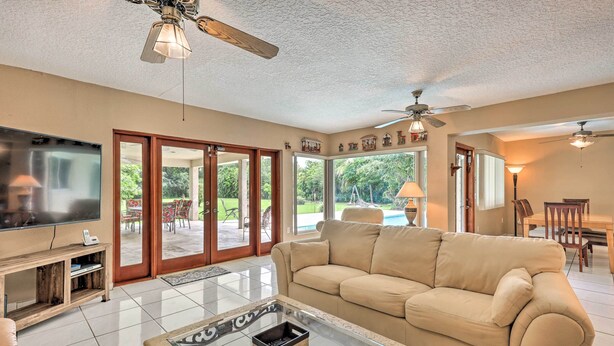 A spacious living room with a beige sofa, a glass coffee table, a flat-screen TV, and a ceiling fan. - Home w/ Pool in Upscale Pinecrest Village (Miami)