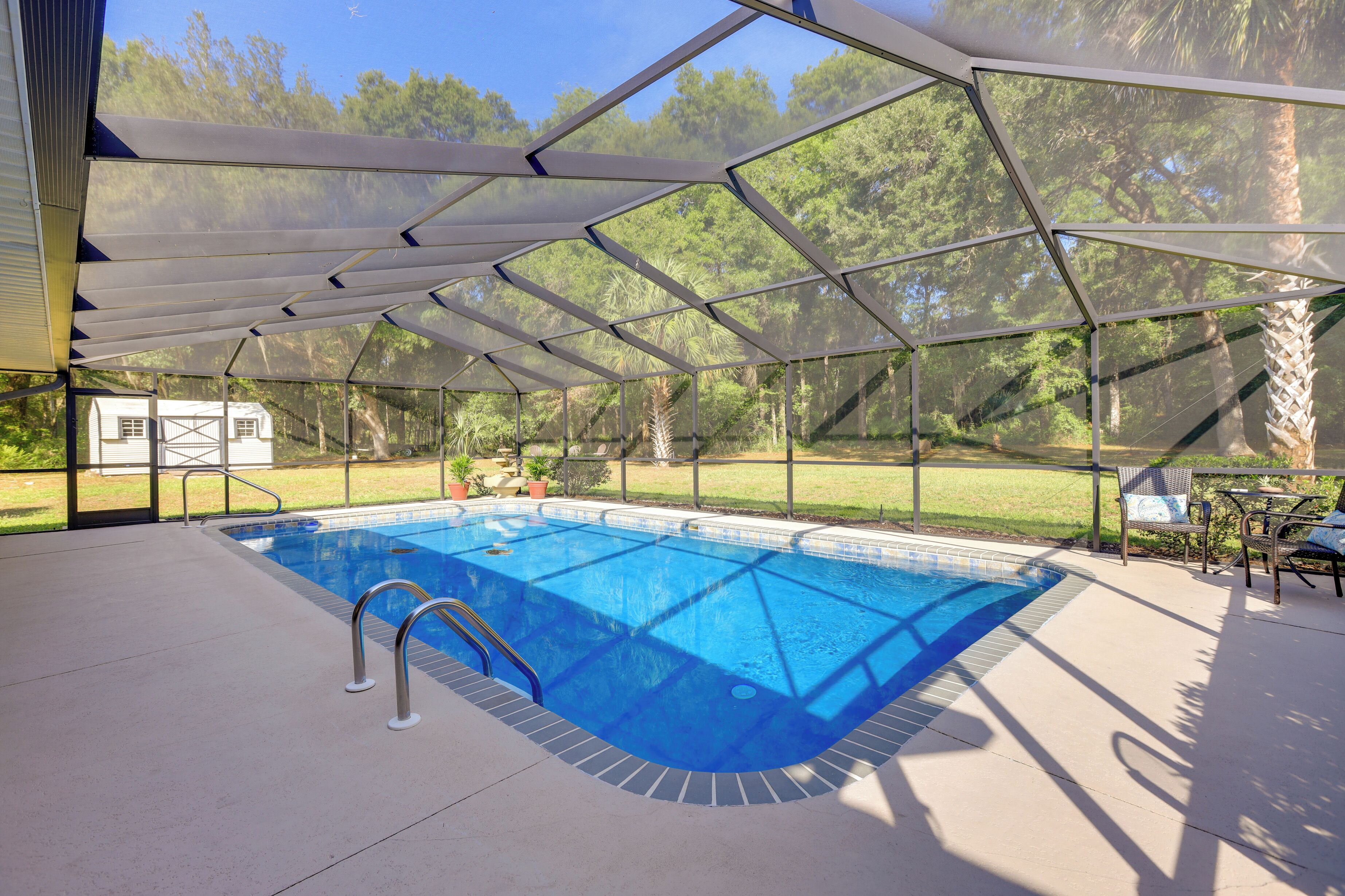 A covered swimming pool with a clear view of the surrounding landscape, including trees and a house in the background.