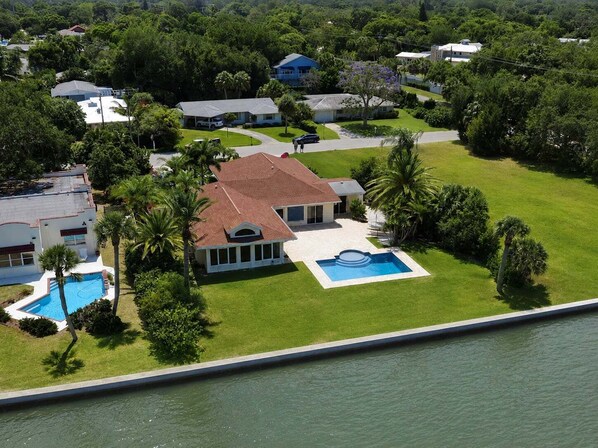 A large house with a swimming pool, surrounded by lush greenery and a body of water.