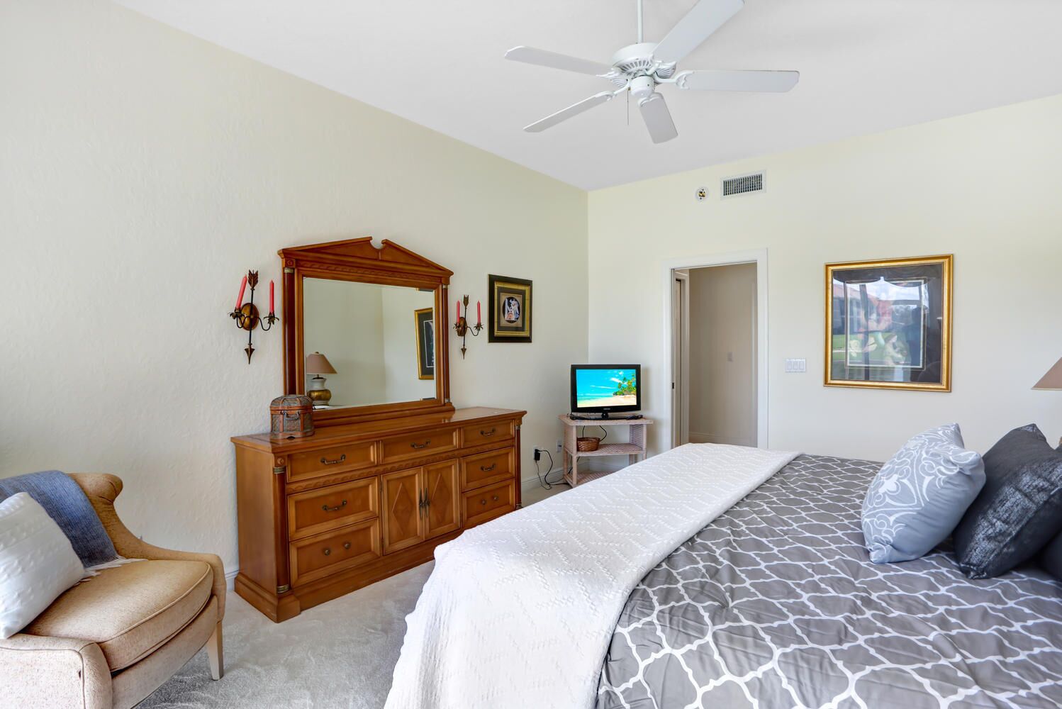 A bedroom with a bed, dresser, television, and a ceiling fan.