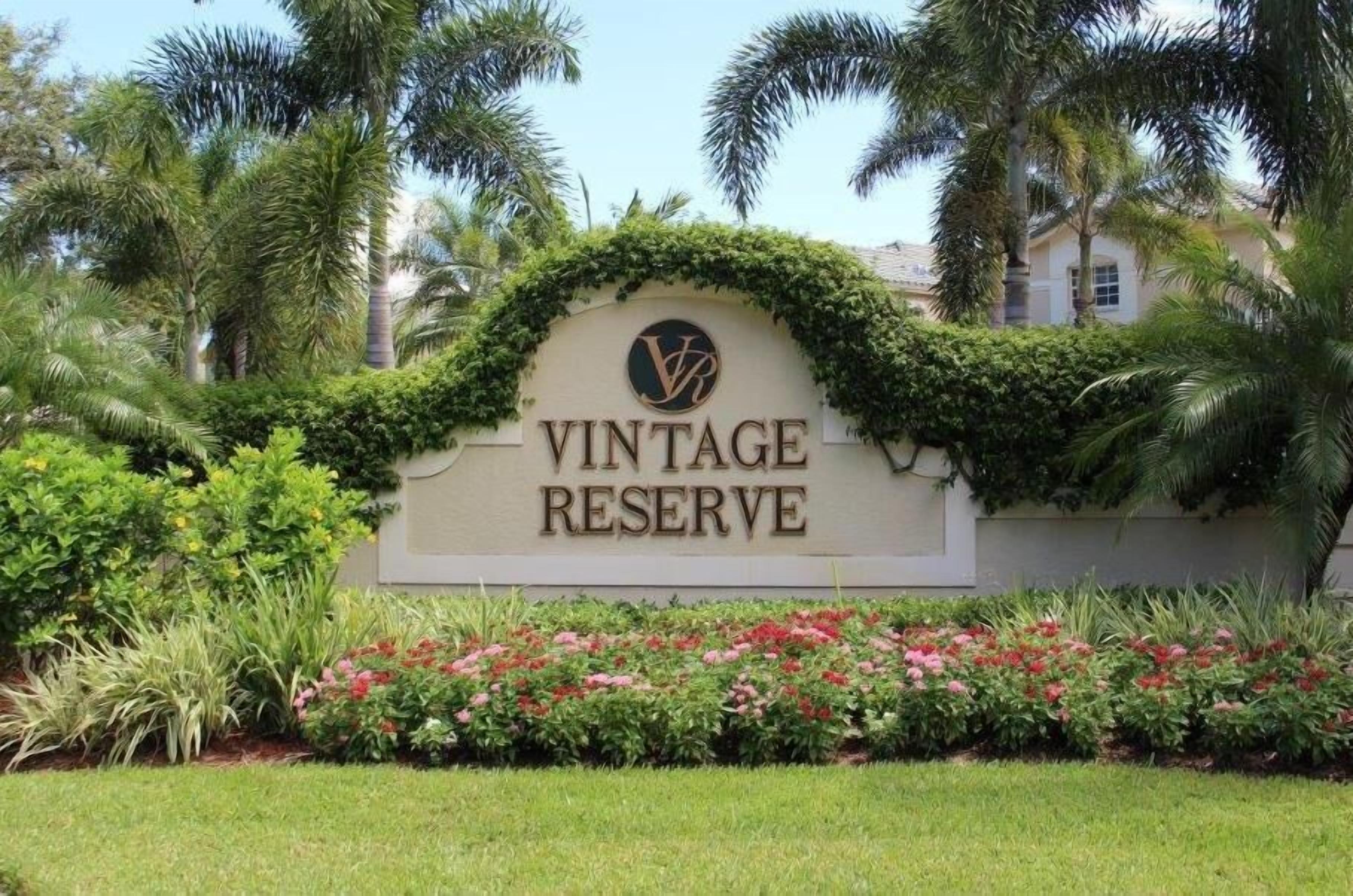 Letrero que dice "VINTAGE RESERVE" con un logotipo, rodeado de exuberante follaje y plantas con flores.