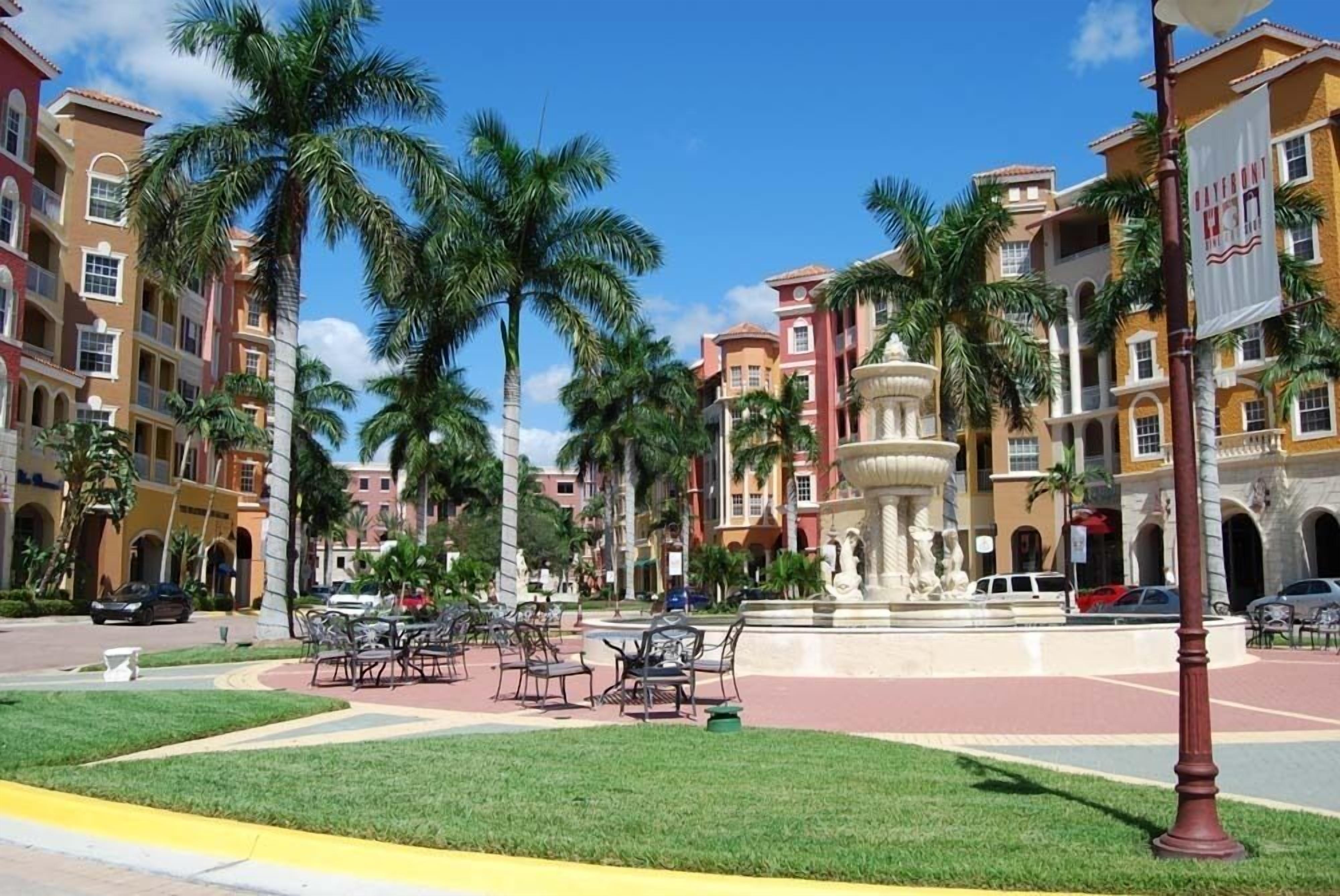 Una plaza con palmeras, mesas al aire libre y una fuente.