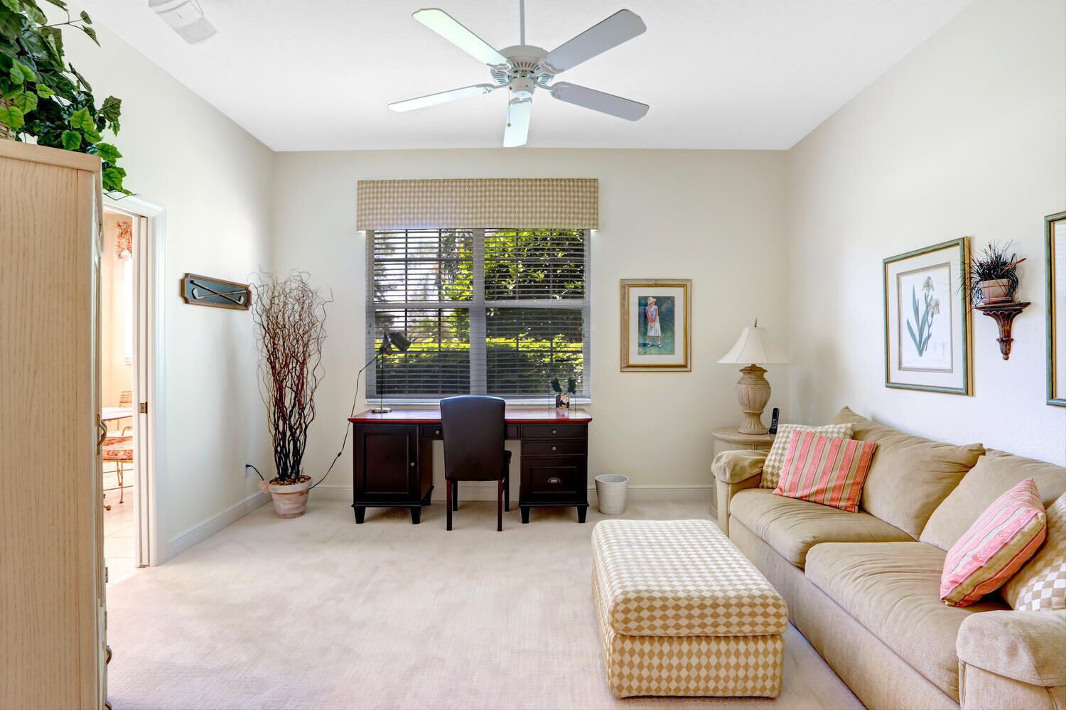 A well-lit room with a desk, a chair, a sofa, and a ceiling fan.
