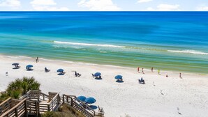 A beach with clear blue water, a sandy shore, and several umbrellas and lounge chairs.