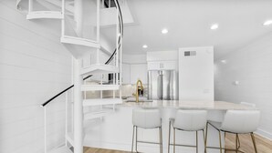 A modern kitchen with a central island, white cabinetry, and a spiral staircase.