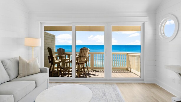 A room with a large sliding glass door leading to a balcony with a view of the ocean.