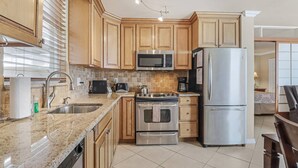 Una cocina moderna con armarios de madera, electrodomésticos de acero inoxidable, encimera de granito y salpicadero de azulejos.