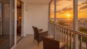 Un balcón con sillas de mimbre, una mesa de vidrio y vistas al atardecer sobre el océano.