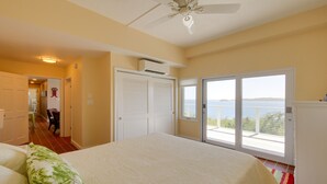 Camera da letto con un letto grande, un ventilatore a soffitto e vista sul mare tramite una porta scorrevole in vetro.
