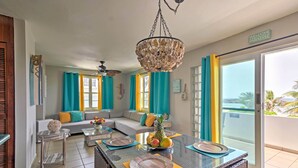 A spacious living room with a large sofa, a dining table set for four, and a balcony with a view.