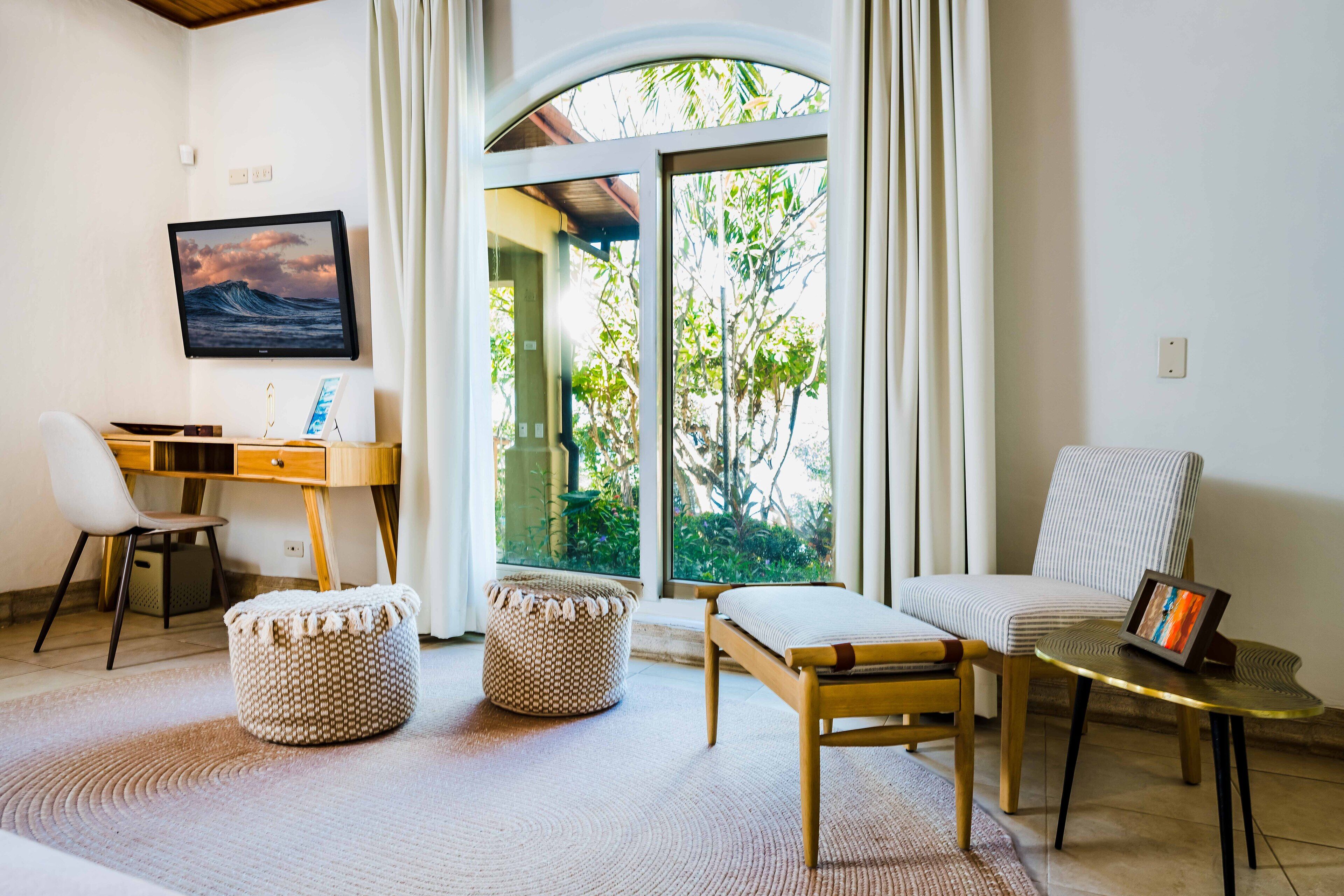 A room with a desk, chair, ottoman, and a sofa.
