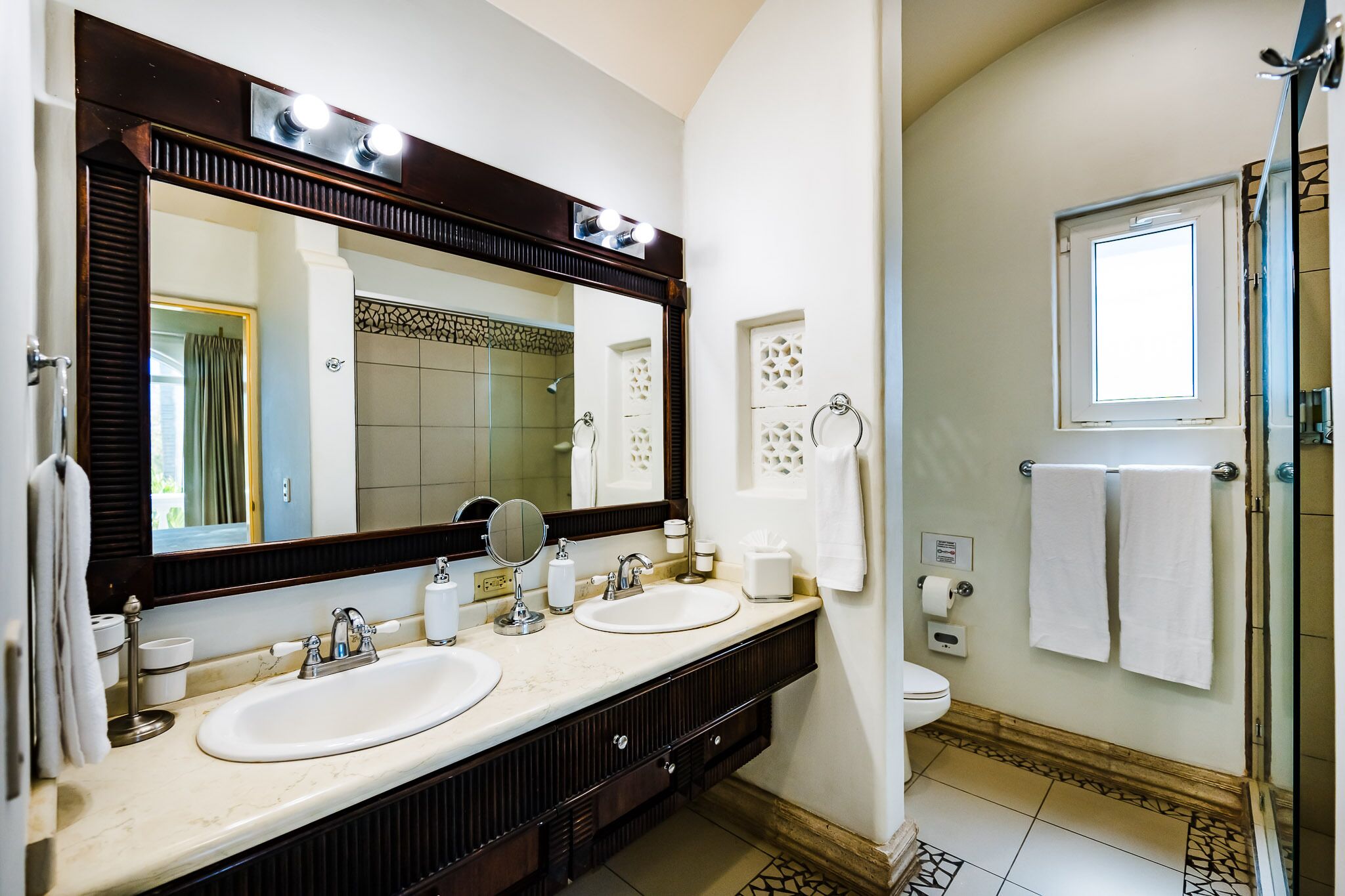 Une salle de bain avec deux lavabos, un grand miroir, des toilettes et une douche.