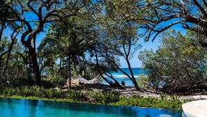 Vista de la piscina con una vista despejada del océano, rodeada de exuberante vegetación y árboles.