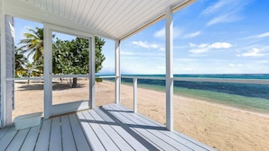 Eine Holzterrasse mit Blick auf einen Sandstrand und Palmen.