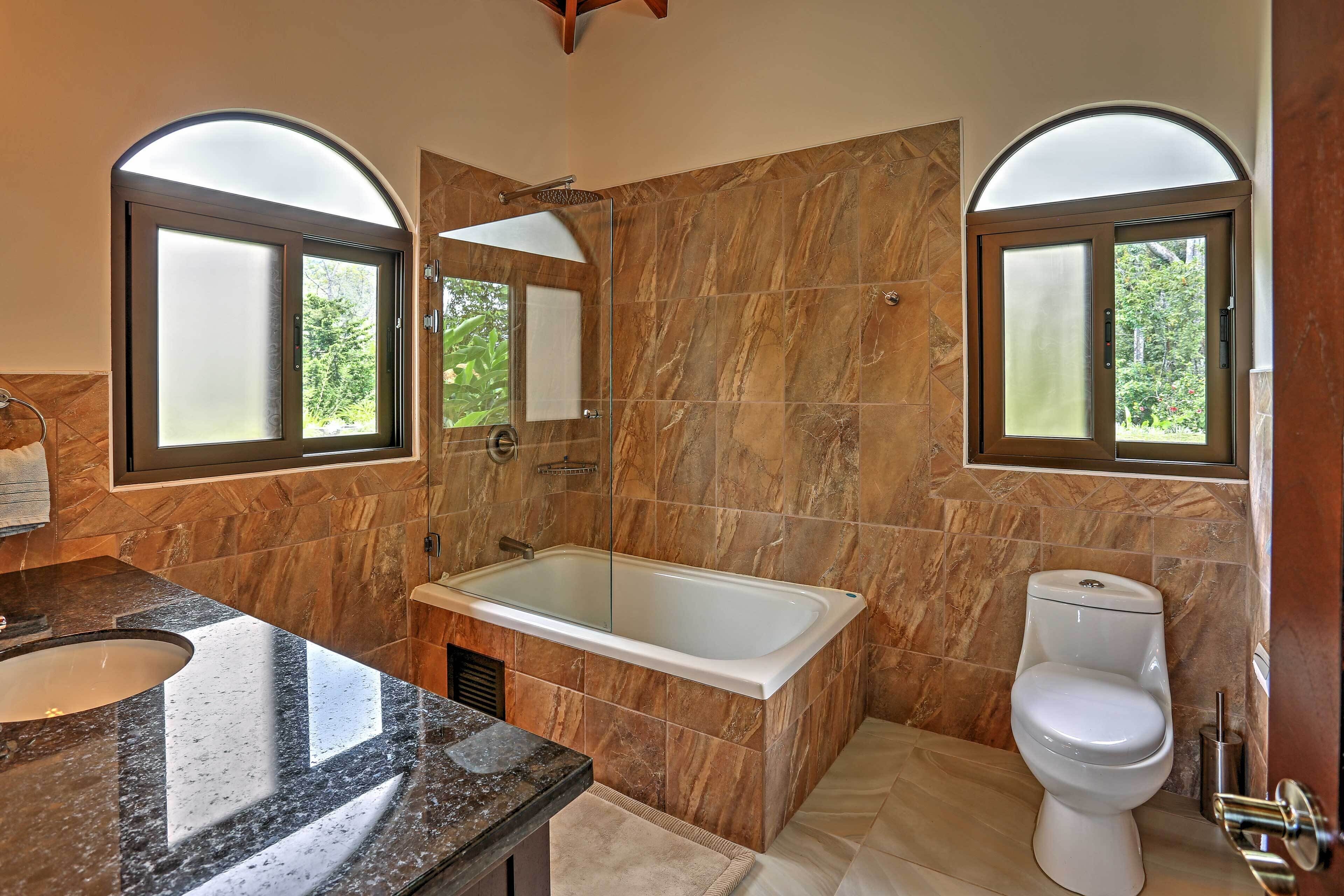 A bathroom with a bathtub, toilet, and a sink. There are two windows with arched tops.