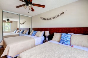 Une chambre d’hôtel avec deux lits, un ventilateur de plafond, un miroir et un élément décoratif mural.