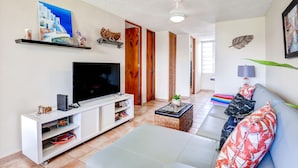 A living room with a flat-screen TV, white entertainment unit, and a sofa with patterned cushions. - Breezy Rio Grande Getaway w/ Pristine Ocean Views! (Rio Grande)