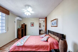 A bedroom with a bed, a ceiling fan, a wooden wardrobe, and a door leading to another room.