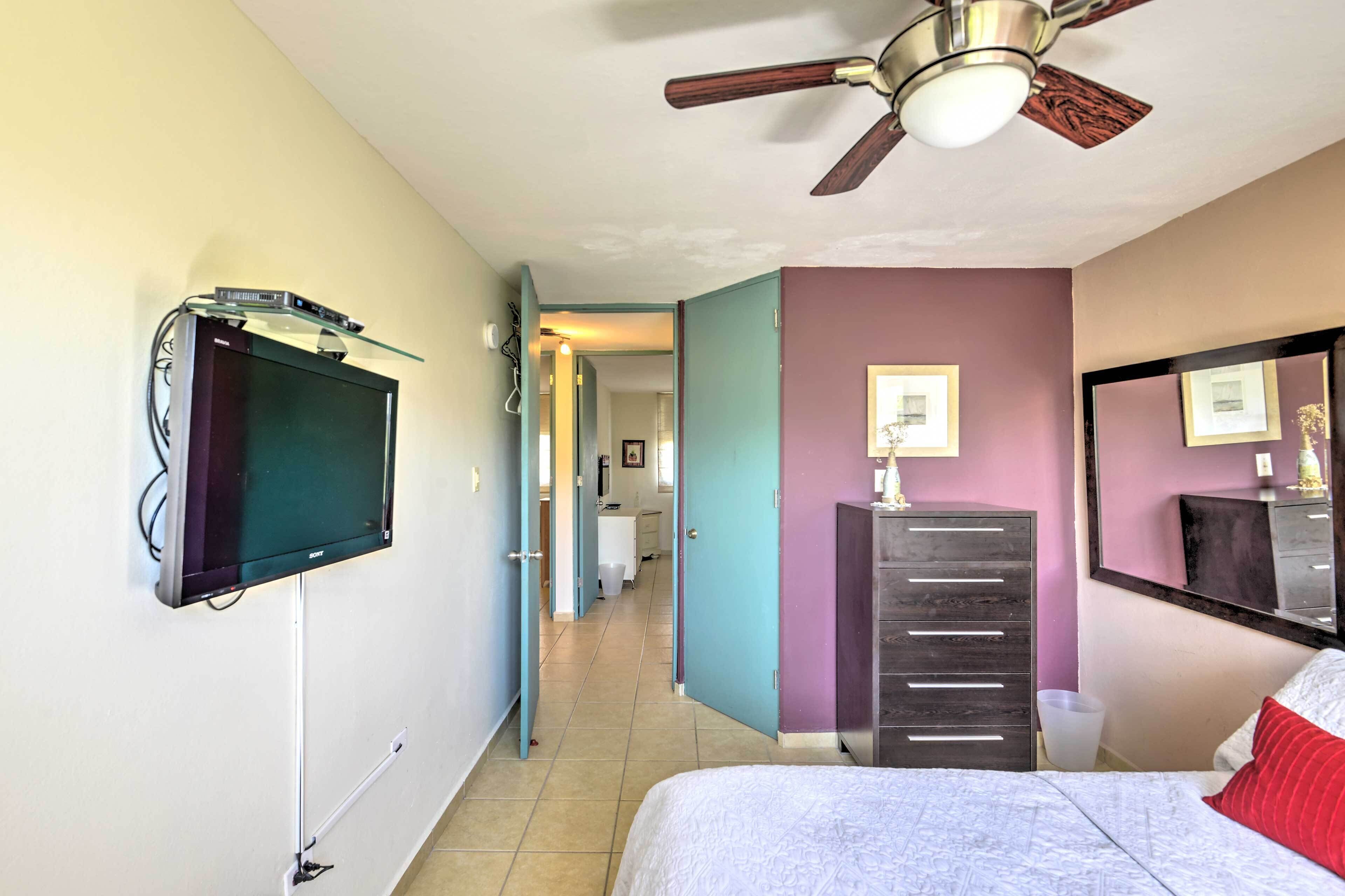 A hotel room with a bed, a ceiling fan, a TV mounted on the wall, a dresser, and a mirror.