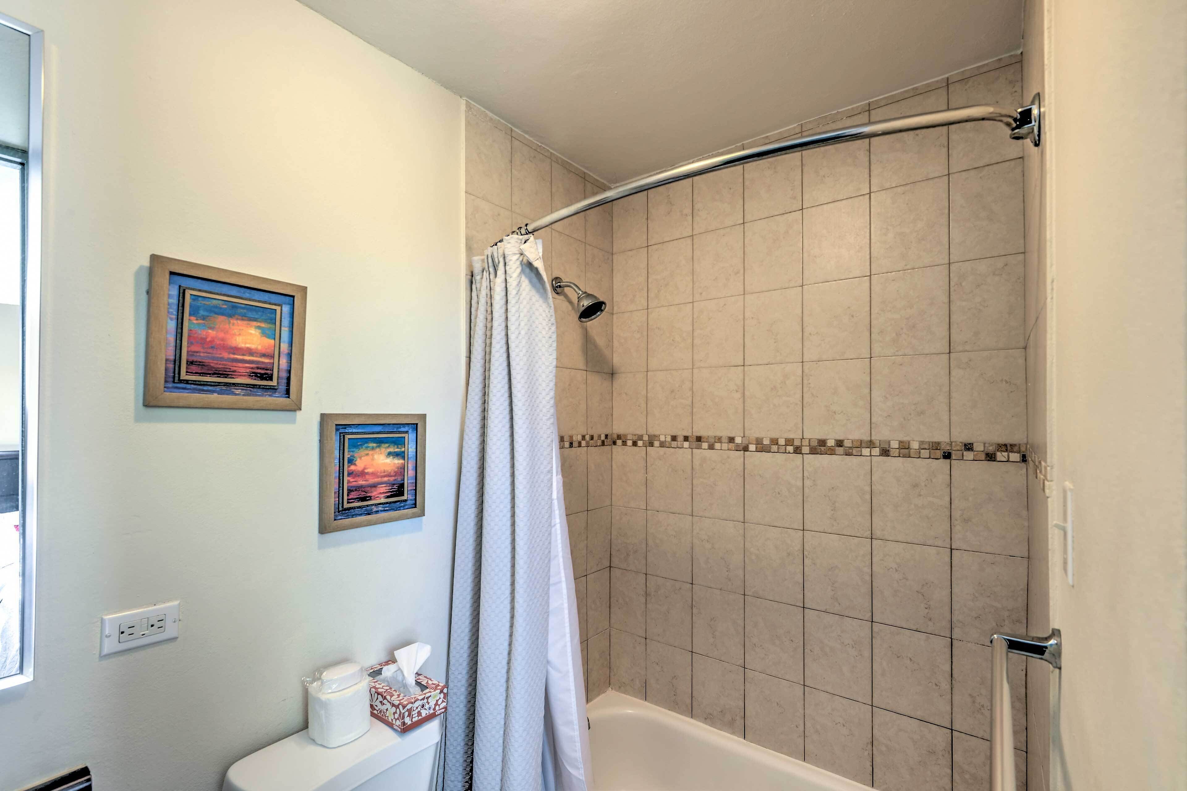 A bathroom with a shower, a toilet, and two framed pictures on the wall.