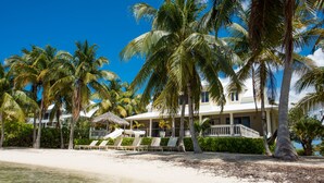 Una propiedad frente a la playa con un edificio blanco, palmeras y una playa de arena.