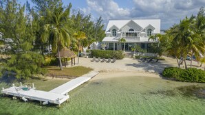 Une propriété située en bord de mer, avec une maison blanche, une eau cristalline et des palmiers.