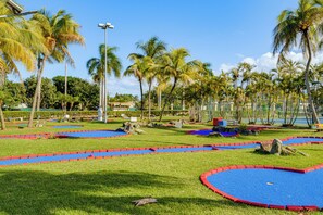 A tropical garden with palm trees, a blue and red play area, and a clear blue sky.