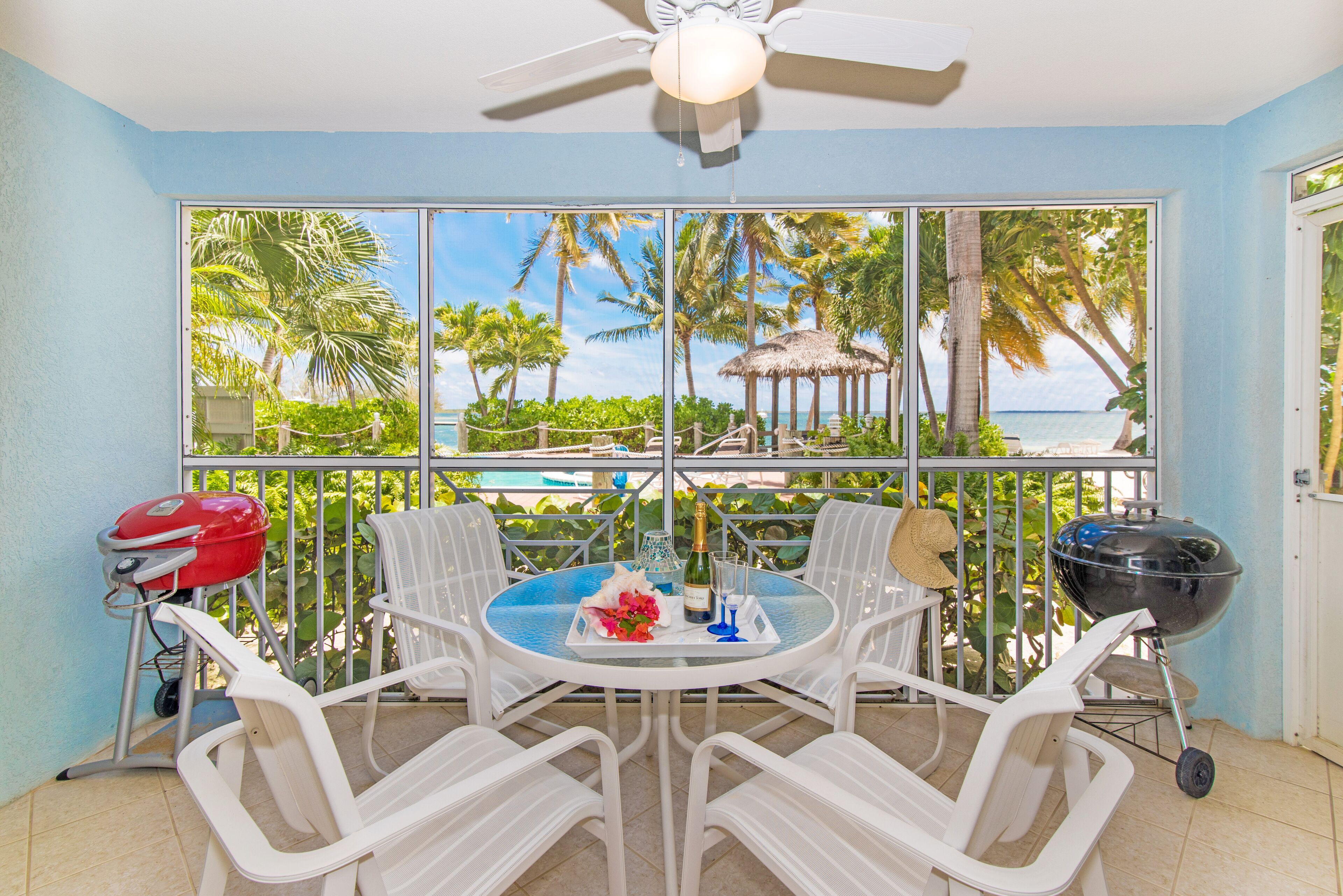A balcony with a table, chairs, a grill, and a view of the beach.