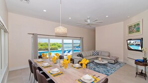 A dining area with a view of a pool and ocean, a gray sofa, and a ceiling fan. - Hidden Cove: Family Hideaway w/Free Kayaks & Bikes, Private Pool and Dock (Cayman Kai)
