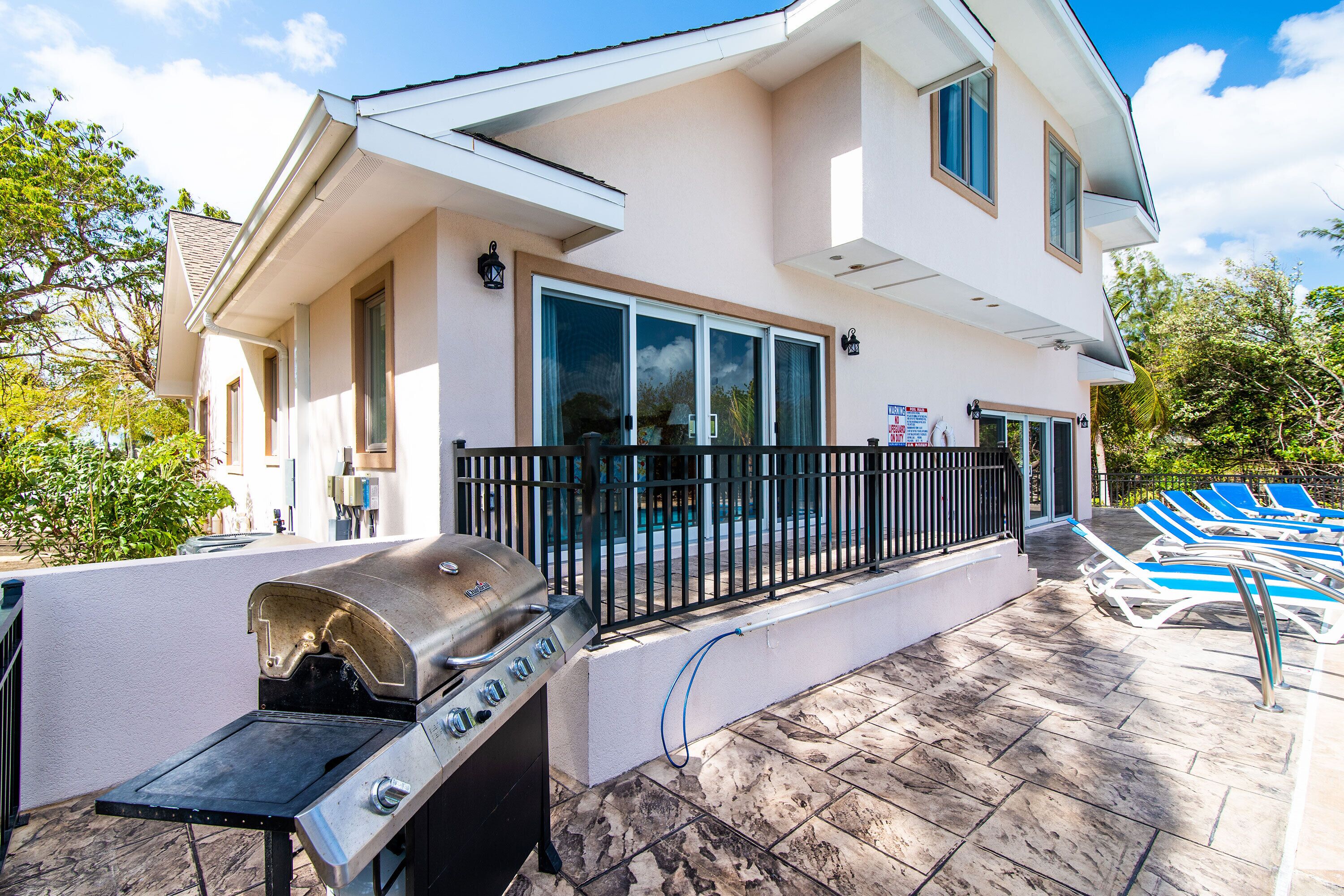 Une maison à deux étages dotée d’un patio comprenant un barbecue, une piscine avec des chaises longues et une terrasse clôturée.