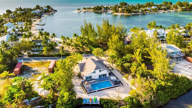 An aerial view of a coastal resort with a swimming pool, beachfront villas, and a marina. - Hidden Cove: Family Hideaway w/Free Kayaks & Bikes, Private Pool and Dock (Cayman Kai)