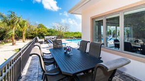 A patio with a pool table, outdoor seating, and a view of the pool and greenery. - Hidden Cove: Family Hideaway w/Free Kayaks & Bikes, Private Pool and Dock (Cayman Kai)