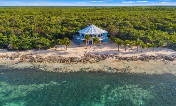 An aerial view of a blue building surrounded by dense green vegetation and clear turquoise waters.