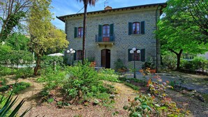 Un bâtiment en pierre doté d’un balcon, entouré d’un jardin où poussent différentes plantes et fleurs.
