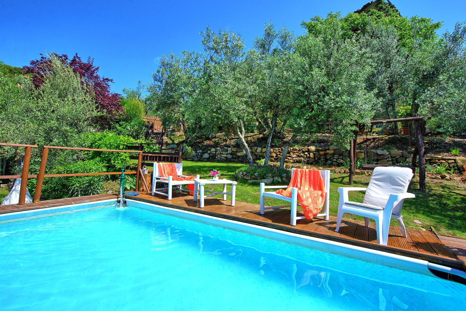 Une piscine entourée de chaises longues blanches et d’une terrasse en bois.