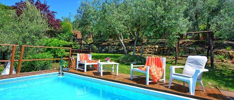Une piscine entourée de chaises longues blanches et d’une terrasse en bois.