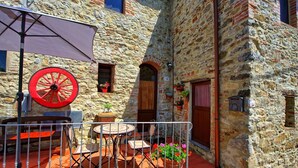 Un edificio in pietra con un balcone, una ruota rossa e posti a sedere all'aperto.