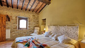 Una camera accogliente con parete in pietra, soffitto in legno, un letto grande con coperta colorata e una finestra vista.