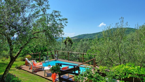 Area piscina con pavimento in legno, sedie a sdraio e vista su un paesaggio montuoso.