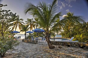 A stone-paved outdoor area with lounge chairs and umbrellas, a pool, and palm trees. - Stunning Caribbean Beachfront Villa on St. Martin! (Les Terres Basses)