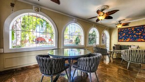 A dining area with a round table and four upholstered chairs, large arched windows with metal bars, and ceiling fans.