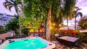 A hot tub surrounded by outdoor furniture, a pool, and a dining area with a view of a building in the background.