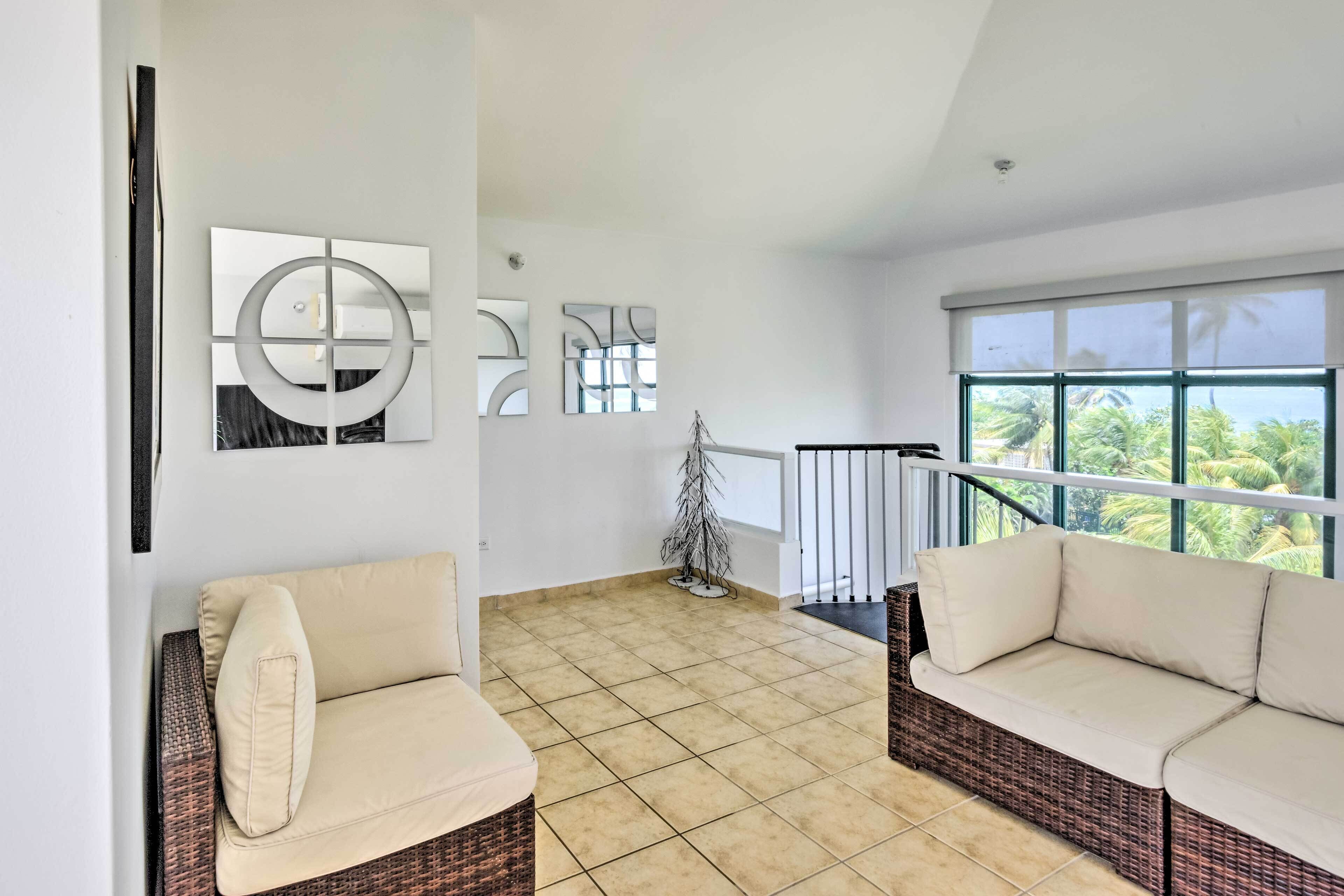 A spacious living area with a large window, a wicker sofa, and abstract wall art.