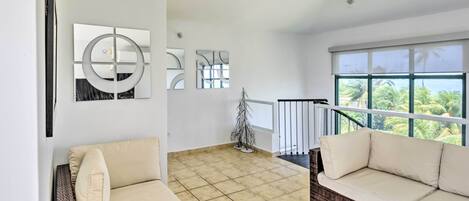 A spacious living area with a large window, a wicker sofa, and abstract wall art.