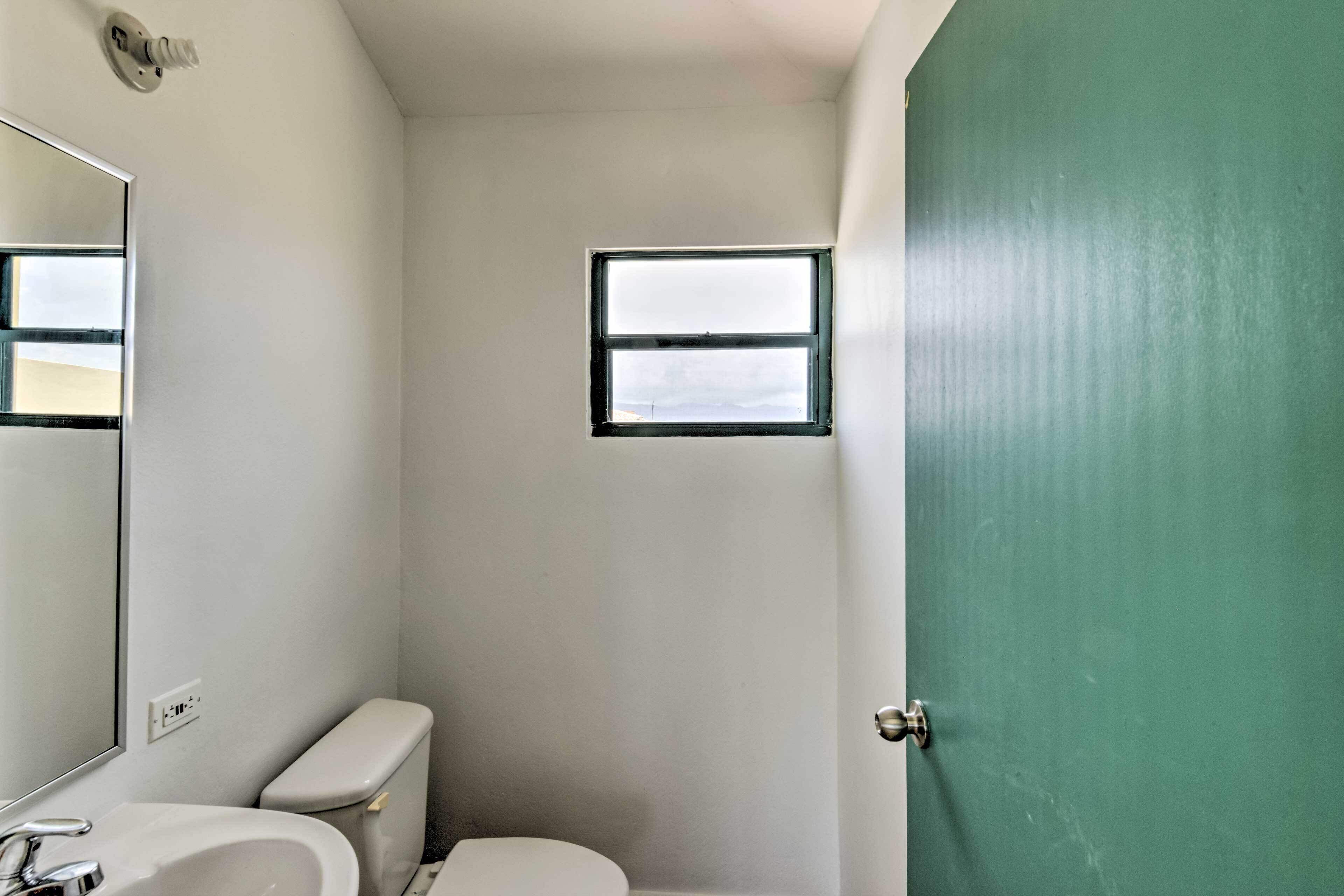 Een kleine, smalle badkamer met toilet, wastafel en een klein raam.