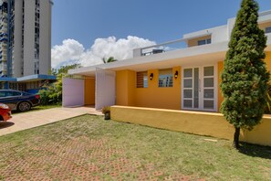 Una casa moderna de dos pisos con fachada amarilla, un porche cubierto y un pequeño jardín.