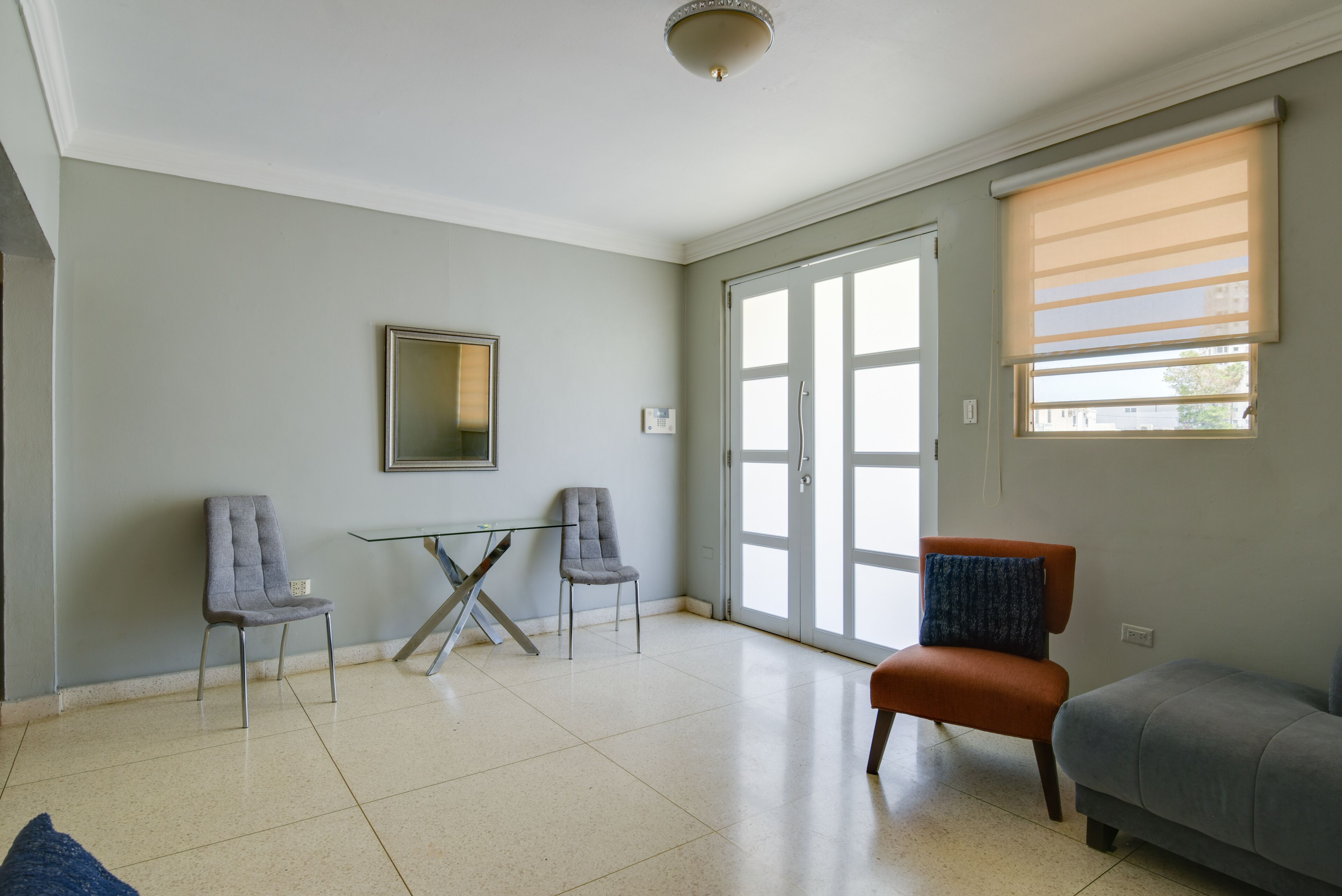 A spacious living room with a glass table, two chairs, a sofa, and a large sliding glass door.