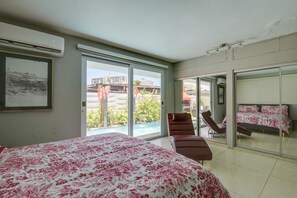 Een slaapkamer met een groot bed, een stoel en uitzicht op een zwembad en gebouwen.