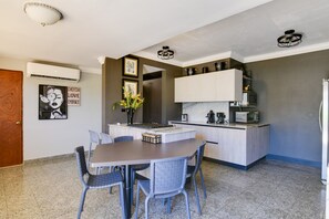 Een kleine keuken met een centraal eiland, witte kasten en een magnetron. Er staat een eettafel met stoelen en een poster hangt aan de muur.