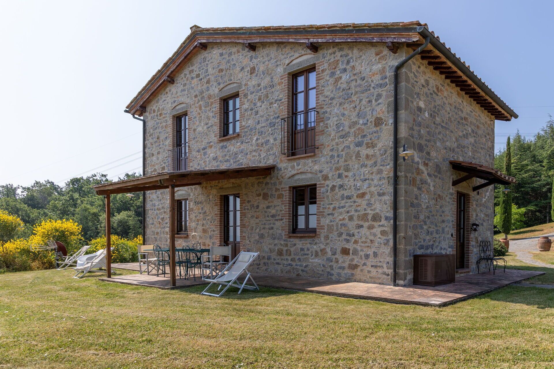 Una casa de piedra con un porche cubierto, un pequeño jardín y mobiliario de exterior.